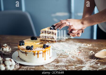 Les mains de la femme coupent le gâteau avec de la crème rose sur le bleu arrière-plan en bois Banque D'Images