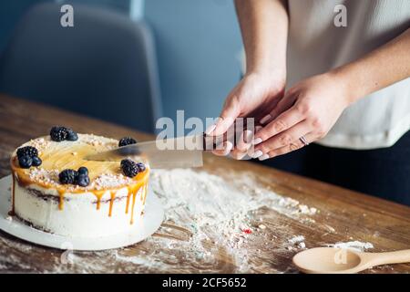 Les mains de la femme coupent le gâteau avec de la crème rose sur le bleu arrière-plan en bois Banque D'Images