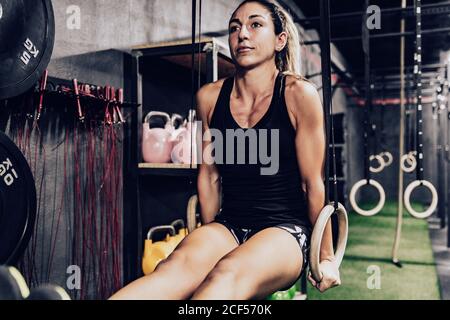 Femme à la forme concentrée effectuant des pull-ups sur des anneaux de gymnastique dans un club de sport Banque D'Images