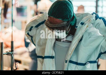 Chirurgien fatigué prenant le masque de protection et l'uniforme pendant le départ salle d'opération après une opération difficile dans une clinique moderne Banque D'Images