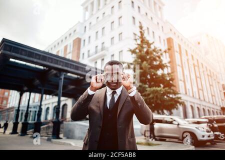 homme d'affaires sérieux à la recherche de l'espace de copie tout en se tenant contre un gratte-ciel en verre, jeune employé professionnel en attente de partenaires internationaux outd Banque D'Images