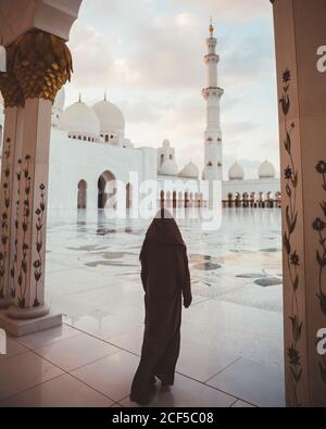 Vue arrière de la femme islamique anonyme en robe noire longue marchant sur la place carrelée de la majestueuse mosquée blanche, Dubaï Banque D'Images