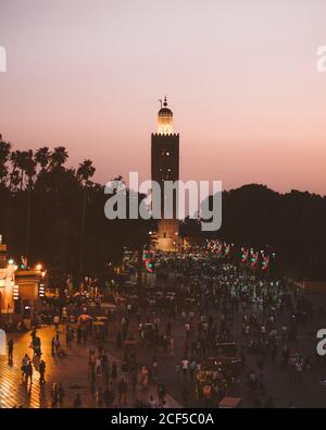 Maroc - avril 08 2019 : foule de personnes anonymes marchant sur la place devant une grande tour d'âge au coucher du soleil Banque D'Images