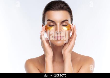 Gros plan portrait de la femme de beauté avec maquillage naturel application de taches d'hydrogel hyaluronic doré sous les yeux. Jeune femme adulte avec une peau propre et fraîche Banque D'Images