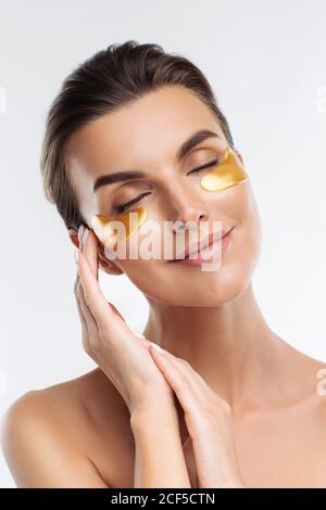 Gros plan portrait de la femme de beauté avec maquillage naturel application de taches d'hydrogel hyaluronic doré sous les yeux. Jeune femme adulte avec une peau propre et fraîche Banque D'Images