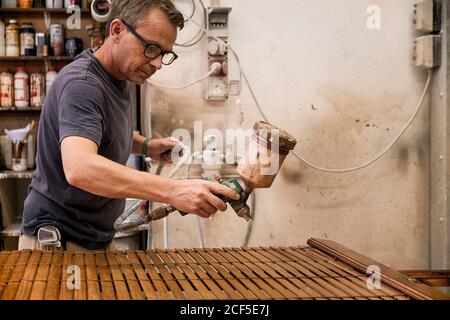 Artisan appliquant du vernis sur le bois jalousie à l'aide d'aérographe en charpenterie atelier Banque D'Images