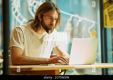 Jeune barbu beau homme assis dans un café à l'extérieur et travaillant tenir le carnet sur une table Banque D'Images