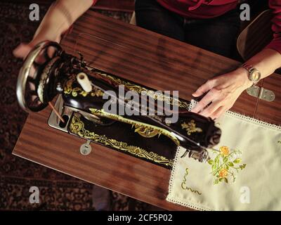 Femme senior en lunettes utilisant une machine à coudre rétro pour créer serviette en lin dans une chambre confortable à la maison Banque D'Images