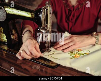 Femme senior en lunettes utilisant une machine à coudre rétro pour créer serviette en lin dans une chambre confortable à la maison Banque D'Images