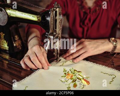 Femme senior en lunettes utilisant une machine à coudre rétro pour créer serviette en lin dans une chambre confortable à la maison Banque D'Images