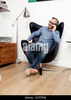homme parlant sur le téléphone mobile souriant ayant une détente café dans le fauteuil à la maison Banque D'Images