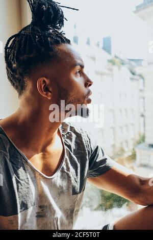 Homme afro-américain attentionné avec des tresses assis à la maison seuil de la fenêtre Banque D'Images