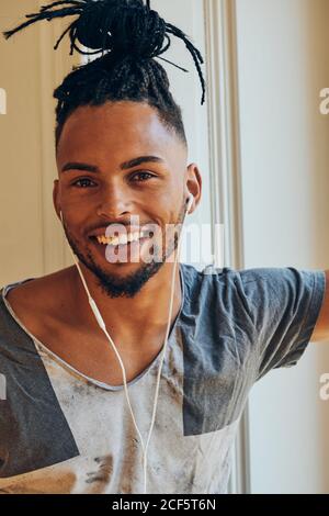 Vue latérale d'un homme ethnique sérieux avec une coiffure créative à l'écoute pour écouter de la musique et vous pencher sur le cadre de la fenêtre Banque D'Images