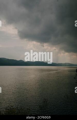 Paysage tranquille avec des rayons de soleil qui brillent à travers des nuages épais lac calme avec eau sombre Banque D'Images