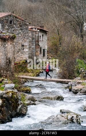 De dessus active femme touriste en veste rouge avec sac à dos lourd traversée voie sur le pont en bois dans le village dans les sommets de l'Europe, Asturies, Espagne Banque D'Images