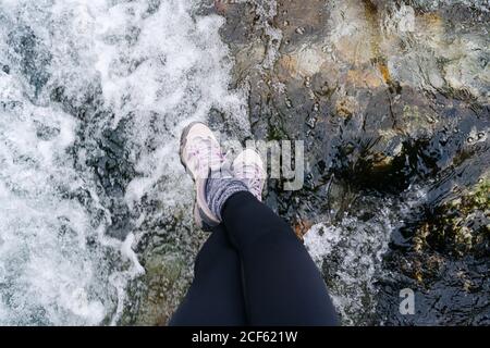 D'en haut de la vue de la petite non reconnaissable décontractée touriste femme dans la veste rouge avec sac à dos assis et jambes pendantes sur le pont en bois dans le village dans les sommets de l'Europe, Asturies, Espagne Banque D'Images