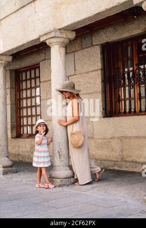 Vue latérale de la femme en chapeau et de l'enfant debout sur le trottoir le long de la vieille maison sur la colonne Banque D'Images