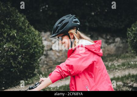 Jeune femme en blouson rouge et casque de protection en vélo à la campagne Banque D'Images