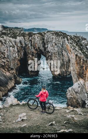 Anonyme jeune femme avec VTT marchant sur la falaise sur fond de mer Banque D'Images