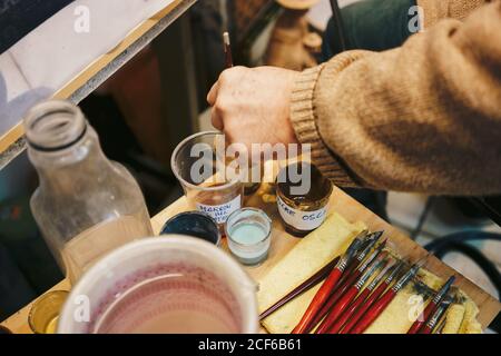 Personne prenant la peinture avec la brosse du verre ayant des outils de dessin autour Banque D'Images