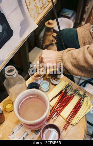 Personne prenant la peinture avec la brosse du verre ayant des outils de dessin autour Banque D'Images