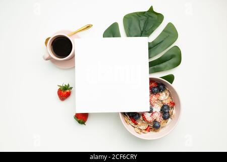 Vue de dessus d'une tasse de café frais et d'un bol avec baies placées sous le papier sur fond blanc Banque D'Images