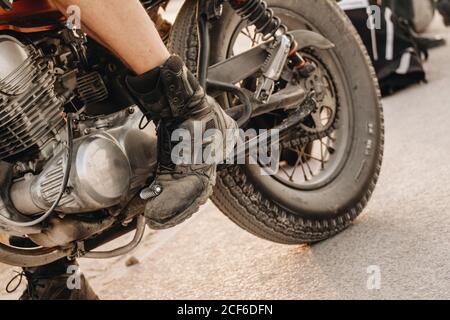 Récolte homme brutal dans des bottes usées en appuyant sur la pédale de boîte de vitesses moto Banque D'Images