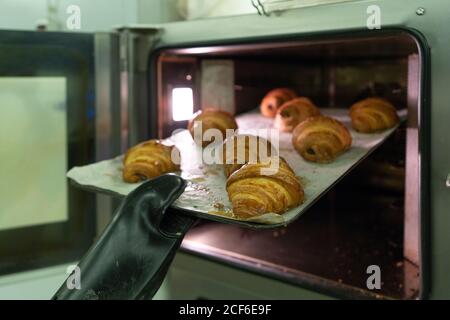 Rognez votre main dans un gant de cuisine noir en tirant hors du four croissants frais à l'intérieur Banque D'Images