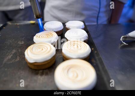 De la cuisson ci-dessus de délicieux gâteaux ronds nappés de crème fouettée caramélisé par une torche à gaz sur la plaque de cuisson Banque D'Images