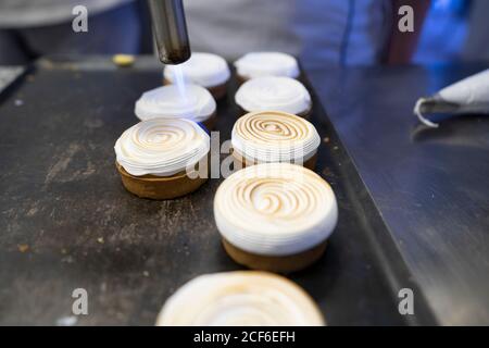 De la cuisson ci-dessus de délicieux gâteaux ronds nappés de crème fouettée caramélisé par une torche à gaz sur la plaque de cuisson Banque D'Images