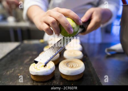 Confiseur de récolte en uniforme blanc décorant de délicieux gâteaux cuits avec zeste de lime dans la cuisine Banque D'Images