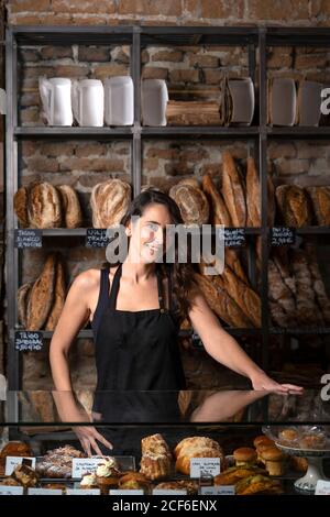 Belle femme en tablier noir vendant la baguette française dans la boulangerie Banque D'Images
