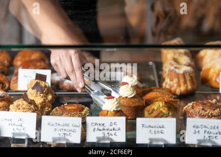 Croiser la main de la personne en prenant la pâtisserie appétissante recouverte de blanc des strongs en métal et crème au comptoir du café Banque D'Images