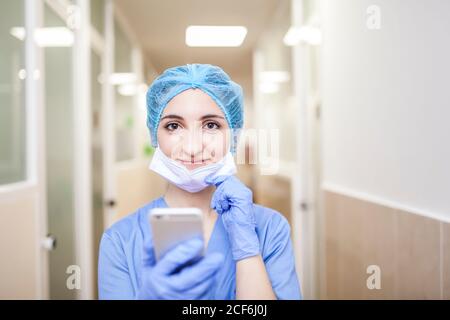 femme chirurgien debout dans le couloir lors de la vérification des messages son smartphone Banque D'Images