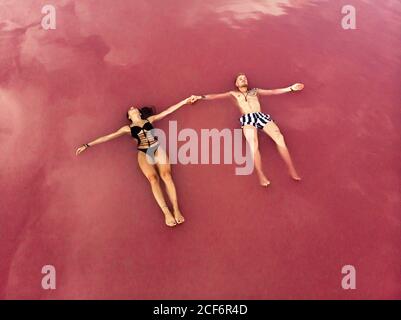 Vue aérienne de l'homme et de la femme paisibles dans les maillots de bain tenant mains tout en flottant sur l'eau salée rose du lac à Torrevieja en Espagne