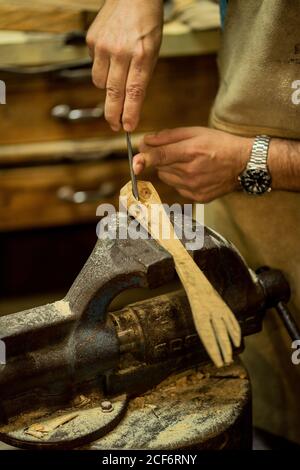 Rognez le menuisier anonyme dans le tablier en utilisant le burin pour faire le trou dans un produit en bois fixé dans un établi lors d'un travail en atelier Banque D'Images