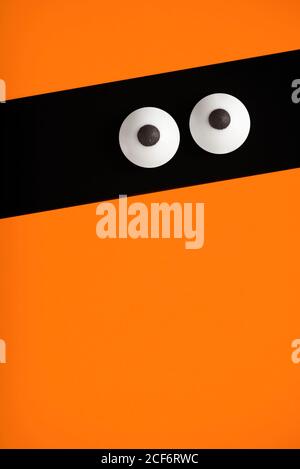 Motif Halloween, deux yeux inclinés dans une bande noire sur fond orange, espace copie. Banque D'Images
