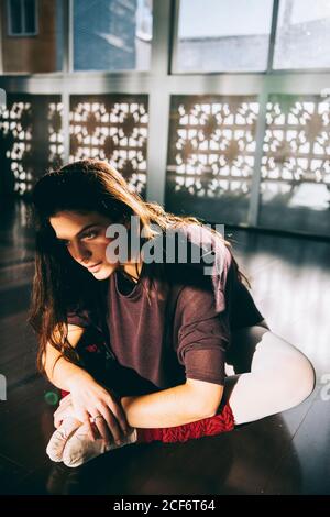 Jeune belle femme se pliant vers l'avant en étirant les jambes tout en étant assise sur le studio à la lumière du soleil. Banque D'Images