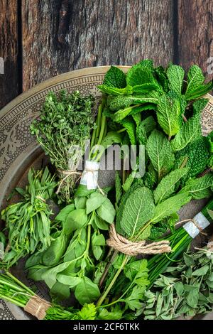 Vue de dessus de la plaque ronde remplie de différents vert frais herbes aromatiques placées sur une table en bois Banque D'Images