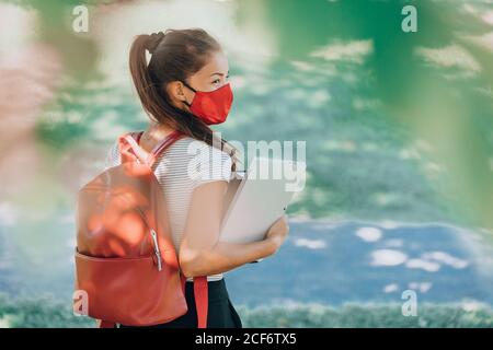 Retour à l'école étudiant de l'université asiatique femme portant un masque de visage sur le campus de marche avec sac à dos rouge, livres et ordinateur portable. Réalité du coronavirus Banque D'Images