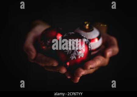 Gros plan personne anonyme démontrant une poignée de boules de Noël décorées contre arrière-plan noir Banque D'Images