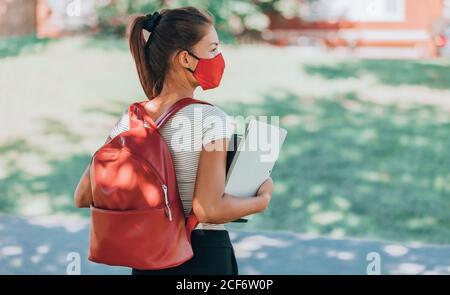 Retour à l'école l'étudiant fille portant un masque covid marchant sur le campus avec sac à dos, livres et ordinateur portable. Virus Corona style de vie Banque D'Images