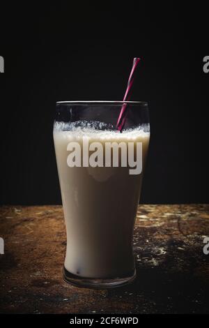 Grand verre de lait blanc avec paille à rayures brillantes tableau sur fond noir Banque D'Images