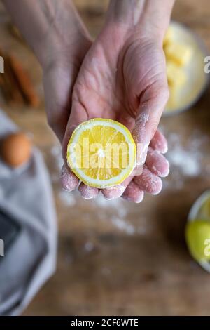 De dessus la main de récolte de femme méconnaissable couverte de farine tenant et montrant à l'appareil photo un citron frais à moitié coupé Banque D'Images