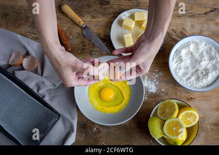 De dessus vue de dessus de dessus de dessus la femelle brisant l'oeuf frais de poulet dans un bol tout en cuisant la pâtisserie dans une table en bois avec ingrédients frais Banque D'Images
