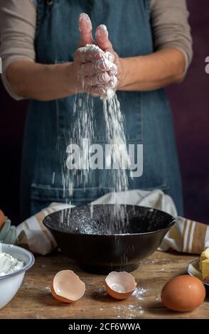 Une femelle non reconnaissable a semé de la farine de blé dans un bol près de l'œuf coquetiers tout en préparant la pâtisserie à la maison Banque D'Images