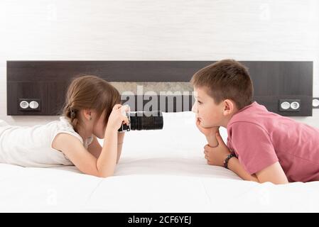 Vue latérale d'une jolie sœur prenant en photo son frère appareil photo en position allongée sur le lit à la maison Banque D'Images