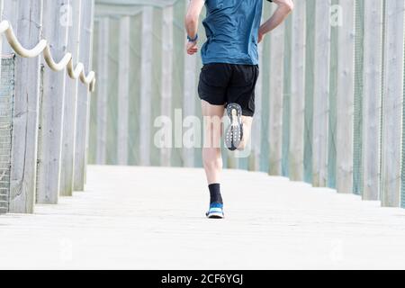 Court sportif masculin non reconnaissable en t-shirt et short bleus courir à l'extérieur sous couvert Banque D'Images