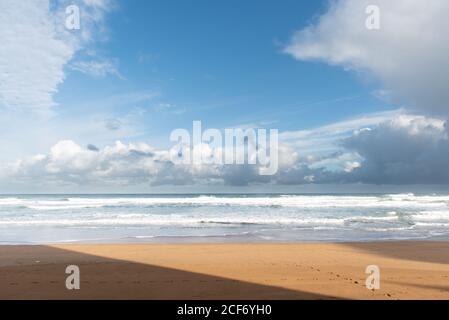Plage de sable vide idyllique le long de l'océan turquoise avec vagues et Mousse sous ciel bleu nuageux à Zarautz en Espagne Banque D'Images