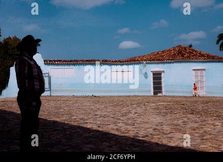 Trinidad, Cuba - 14 DÉCEMBRE 2019 : vue latérale d'un homme adulte méconnaissable en chapeau de cow-boy debout près d'une maison rurale bleue par beau temps Banque D'Images